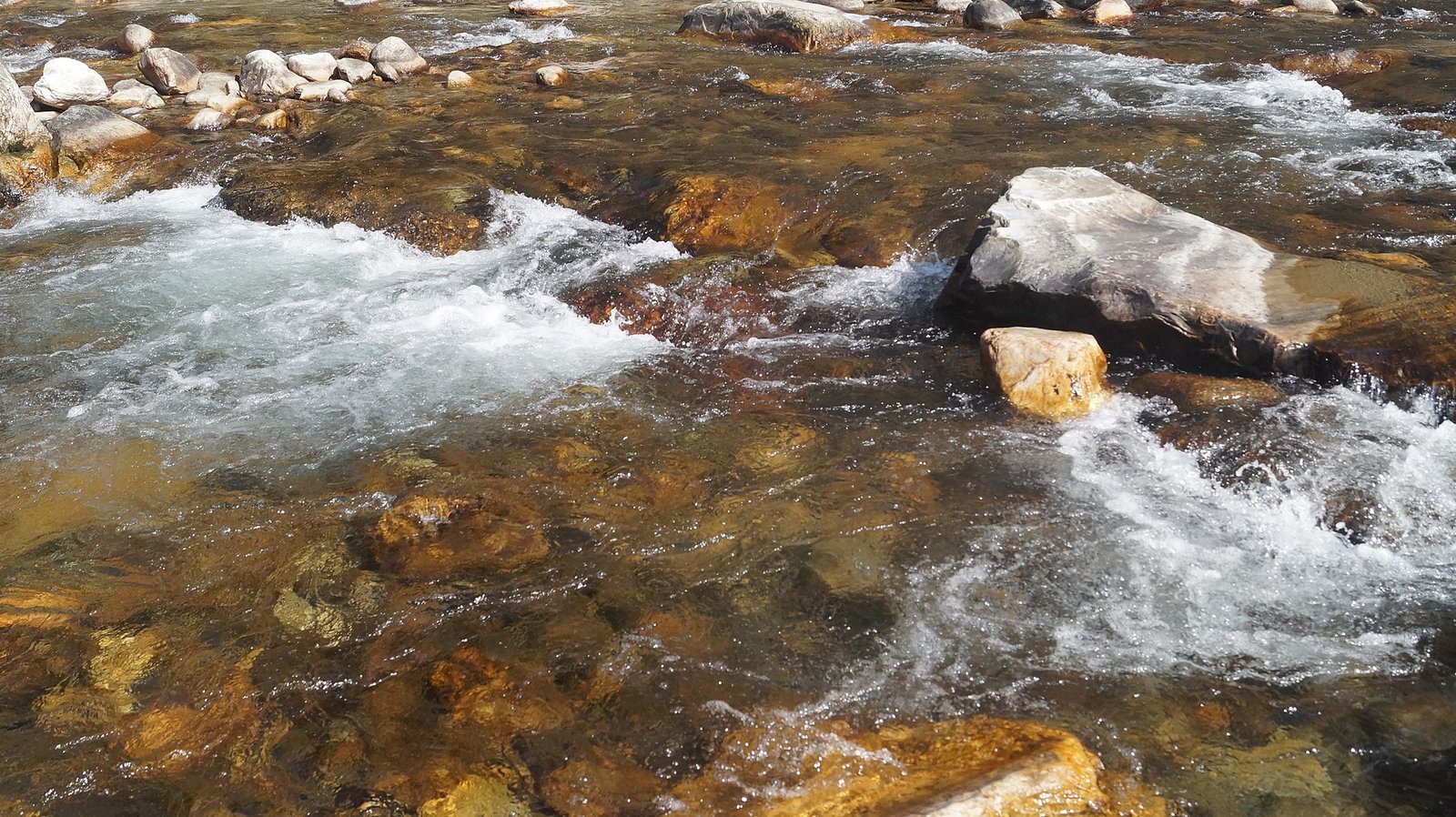Clear shallow water of the Tirthan river running over pale rounded stones