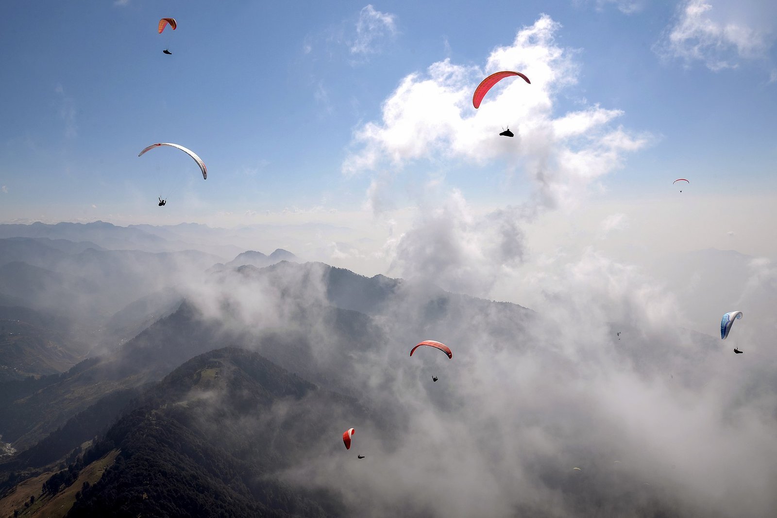 Six paragliders soaring above cloud-wrapped forested ridges of the Dhauladhar foothills at Bir Billing